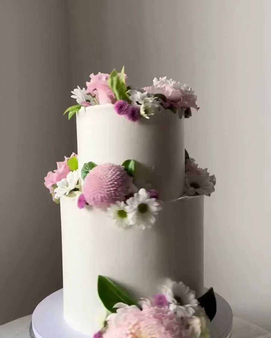 A two tier white buttercream cake dressed with fresh pink and white flowers